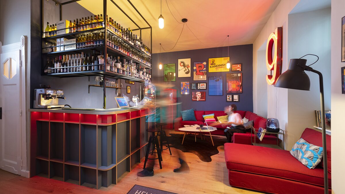 A colourful design studio lounge with a red sofa, bar shelves and framed posters on the walls.