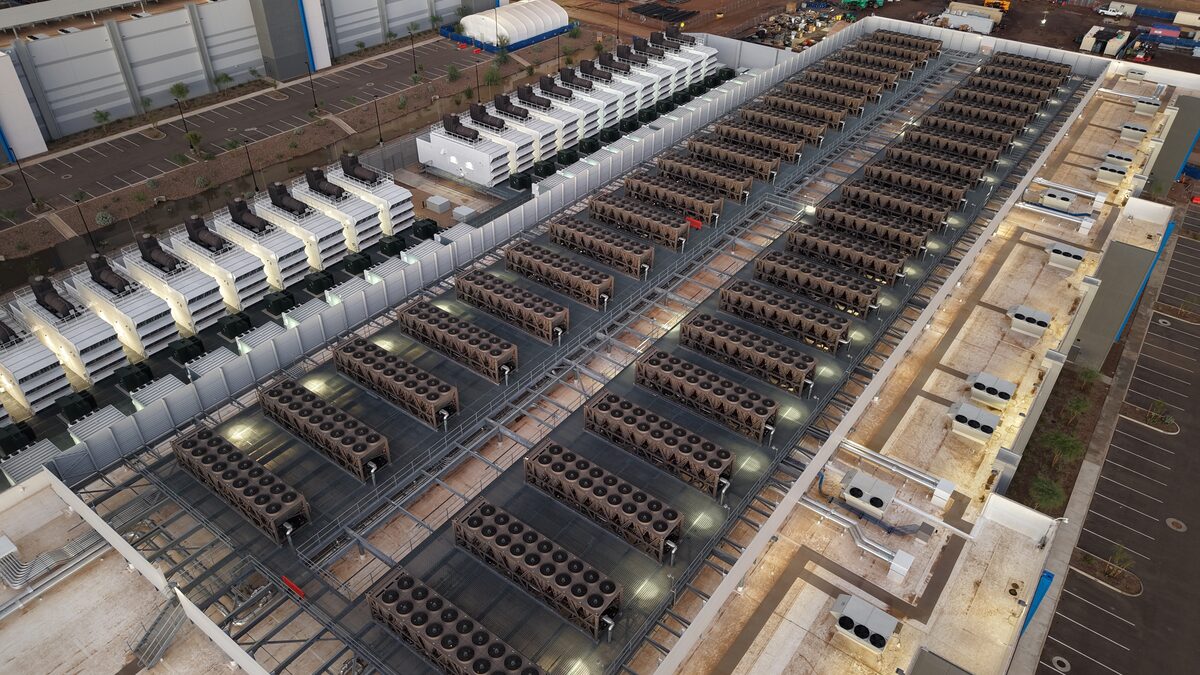 Cooling units and backup generators lined up on the roof of a large data centre at dusk.